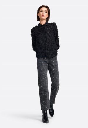 Schwarze Kunstfelljacke mit hohem Kragen, Knopfleiste, kombiniert mit dunklen Jeans mit silbernen Nieteinsätzen und spitzen schwarzen Stiefeletten.