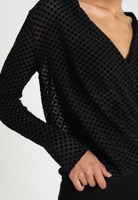 Top a maniche lunghe nero con un motivo a pois in tessuto trasparente, scollatura a V profonda e vestibilità rilassata.