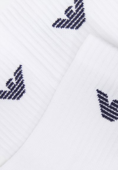 Calcetines blancos con textura acanalada que presentan diseños de corazones a rayas en color azul oscuro a los lados. El tejido parece suave y elástico.