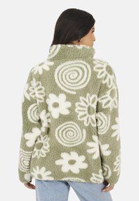 Giacca in pile verde oliva con motivi floreali e spirali bianchi. Presenta un colletto alto e una finitura morbida e strutturata.