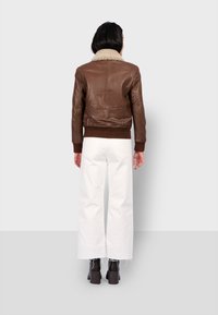 Chaqueta bomber de cuero marrón con un suave cuello beige, puños y dobladillo acanalados, que presenta un diseño elegante y una textura suave.