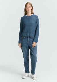 Maglione blu lavorato a maglia con un design testurizzato e a motivi, abbinato a jeans azzurri chiari e sneakers bianche. Il maglione ha un collo rotondo.