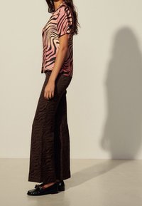 Chemise à rayures roses et noires à manches courtes avec un col, assortie à un pantalon marron présentant un motif ondulé similaire et des mocassins noirs.