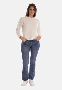 Maglione a maglia crema con collo rotondo, abbinato a jeans a zampa d'elefante blu e sneakers bianche. Il maglione ha maniche lunghe e una vestibilità comoda.