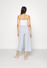 Wit cropped top met dunne bandjes, gecombineerd met lichtblauwe gestreepte brede broek. Model draagt witte sandalen, zicht vanaf de achterkant.