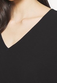 Svart V-ringad topp gjord av glatt tyg; närbild visar mjuk textur och rena sömmar längs halsringningen.