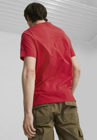 Czerwona koszulka z krótkim rękawem, uszyta z bawełny, z okrągłym dekoltem i małym czarnym logiem na rękawie, zestawiona z oliwkowymi spodniami cargo.