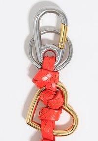 Czerwony pleciony skórzany breloczek z złotym sercowym akcentem i srebrnym karabińczykiem. Skóra ma teksturowane, błyszczące wykończenie.