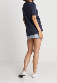 Námořnická košile s krátkým rukávem, volný střih, v kombinaci s světle modrými džínovými šortkami s třásněmi a bílými plátěnými teniskami.