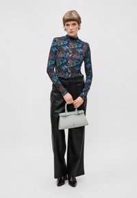 Langärmliges Oberteil in Schwarz mit lebhaftem Blumenmuster, kombiniert mit schwarzen Lederhosen und einer grauen Handtasche. Glatte Texturen und straffes Design.