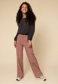 Lichte zwarte top met lange mouwen en een geplooide halslijn, gecombineerd met roze wijde broekspijpen met voorzakken en knoopsluiting.