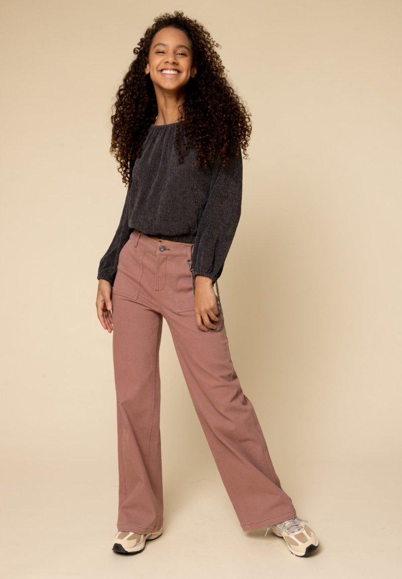 Lichte zwarte top met lange mouwen en een geplooide halslijn, gecombineerd met roze wijde broekspijpen met voorzakken en knoopsluiting.