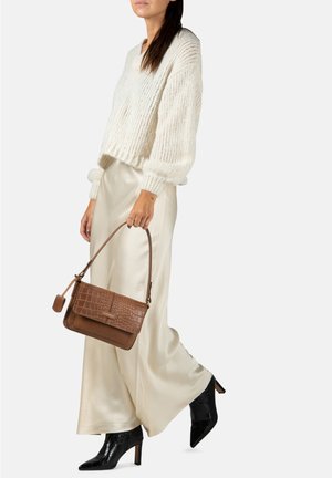 Pull en tricot blanc, jupe en satin beige, bottes à talons hauts en cuir noir gaufré crocodile et sac à main marron en motif crocodile.