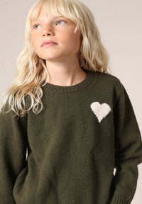 Olijfgroene gebreide trui met een witte hart op de linkerborst, geribbelde kraag en lange mouwen met een gezellige textuur.
