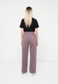 Pantaloni cargo a gamba larga in morbido lavanda, realizzati in cotone resistente, con molteplici tasche e un design a vita alta, abbinati a una t-shirt nera.