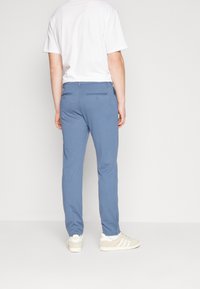 Jasnoniebieskie spodnie o dopasowanym fasonie, z dwoma tylnymi kieszeniami i minimalistycznymi detalami przeszyć, zestawione z białym t-shirtem i jasnym obuwiem.