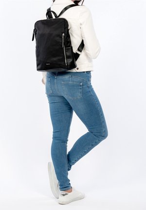 Sac à dos noir en matériau lisse, avec deux poches zippées, des bretelles ajustables et un design minimaliste. Idéal pour un usage quotidien.