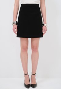 Zwarte A-lijn rok met een gladde textuur, aansluitende taille en subtiele zijnaad. Gepaard met glanzende zwarte stilettohakken en zilveren armbanden.