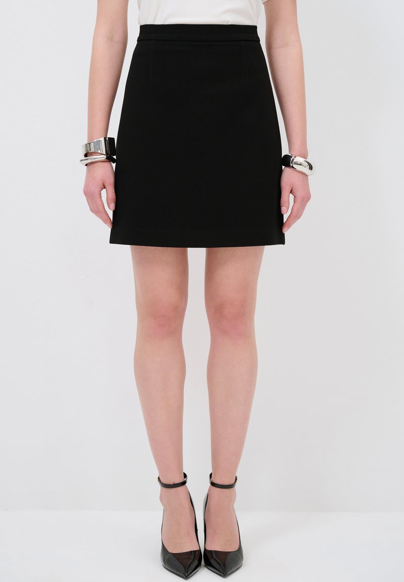 Zwarte A-lijn rok met een gladde textuur, aansluitende taille en subtiele zijnaad. Gepaard met glanzende zwarte stilettohakken en zilveren armbanden.