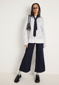 Ανοιχτό γκρι oversized πουλόβερ με ναυτικές ρίγες, σκούρες φαρδιές τζιν, γκρι κάλτσες και μαύρες χοντρές μπαλαρίνες. Μικρή μαύρη τσάντα και γυαλιά ηλίου.