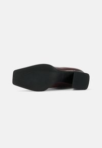 Black rubber sole with textured pattern. Wine-colored upper in smooth material, featuring a sleek, rounded toe and a modest block heel.