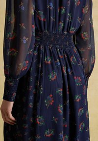 Tumes lilleline kleit õhukeses kangas, millel on värvilised lillemustrid, smockitud vöökoht ja puhv-ningadega varrukad, mis on kitsendatud mansettidega.