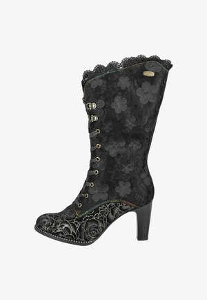Bottine noire avec un superposé de dentelle florale, bord supérieur festonné et motifs floraux en relief. Dotée d'un talon haut et de détails de couture décoratifs.