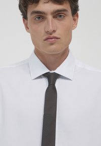 Chemise blanche à col classique, associée à une cravate gris foncé avec un motif à pois. Tissu lisse avec une coupe structurée.