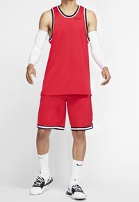 Red sleeveless athletic tank top and matching shorts, featuring black and white accents. Worn with white arm sleeves and black sneakers.