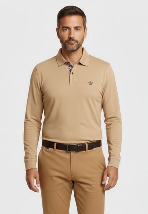 Camisa polo de manga larga color beige con un cuello estampado, que presenta un logotipo en el pecho. Combinada con pantalones beige y un cinturón marrón.