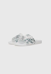 White slide sandals with a decorative blue and gray floral pattern on the strap, featuring a textured footbed and flat sole.