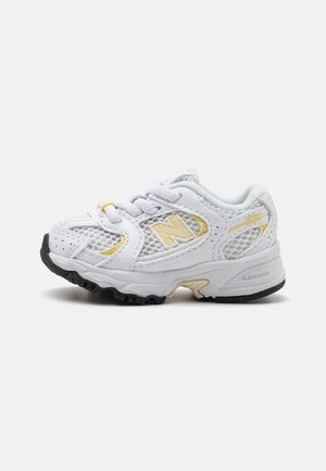 Baskets pour tout-petits blanc et jaune clair avec mesh respirant, logo New Balance, semelle rembourrée avec talon et avant à empreinte noire.