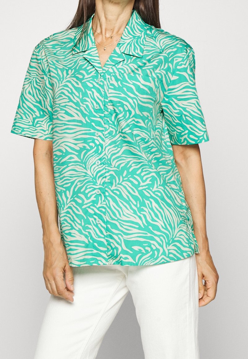 Chemise à manches courtes en turquoise avec des rayures zèbre blanches. Dotée d'un col classique et d'une fermeture à boutons, fabriquée en tissu léger.