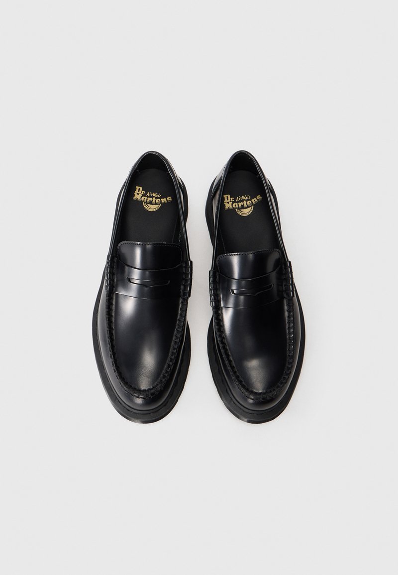 Un paio di mocassini in pelle nera lucida Dr. Martens con suole spesse, dettagli di cuciture a vista e plantari con marchio su uno sfondo bianco semplice.