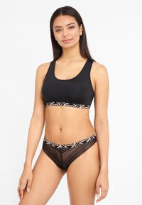 Schwarzer Sport-BH mit einem gemusterten elastischen Band und passenden schwarzen Spitzenslips. Glatte Textur, figurbetontes Design, dezente dekorative Akzente.