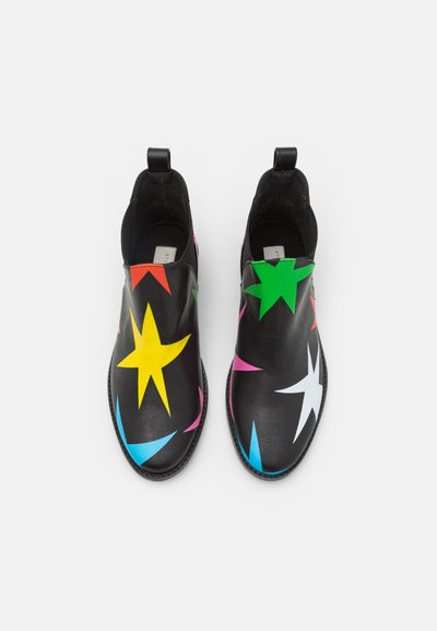 Scarpe slip-on nere con motivi a stelle colorati in giallo, verde, rosa, blu e bianco. Texture in pelle liscia con una leggera lucentezza.