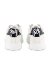 Bijele kožne tenisice s crnim lakiranim petnim dijelom koji sadrži logotip "KARL LAGERFELD KIDS", okrugli vrh i debeli bijeli potplat.