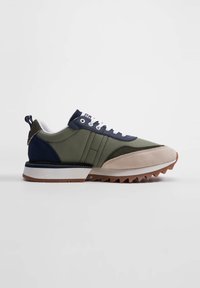 Scarpa da uomo con tela verde oliva, dettagli blu navy, punta in camoscio beige, lacci bianchi e suola in gomma testurizzata con bordi seghettati.