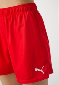 Punase punased sportlikud lühikesed püksid, mis on valmistatud kergest kangast ja painduva vöökohaga. Vasakul jalal on valge Puma logo.