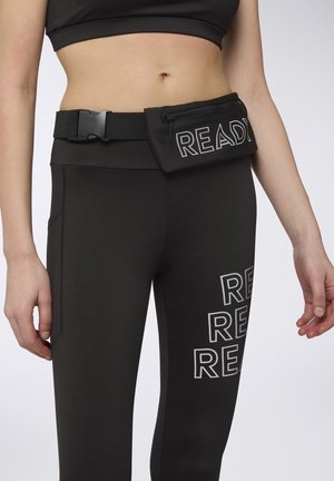 Leggings sportive neri con la scritta "READY" in bianco, indossati con una cintura a sacchetto nera con zip abbinata. Texture liscia, design aderente e finiture senza cuciture.