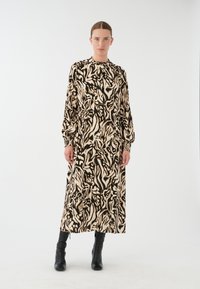 Langärmliges Midikleid in einem cremefarbenen und schwarzen abstrakten Muster, mit hohem Ausschnitt und elastischen Manschetten, kombiniert mit schwarzen Stiefeletten.