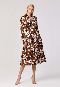 Robe midi à fleurs marron avec des manches longues, un devant boutonné et une jupe évasée. Présente des motifs de fleurs blanches et roses sur un fond sombre.
