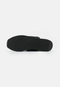 Schwarze Sneaker-Sohle aus strukturiertem Gummi, mit horizontalen Rillen für Traktion und einem glatten Heel-Design.