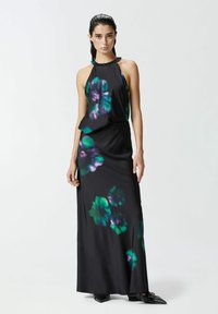 Robe maxi sans manches noire avec un motif floral vert et violet. Fabriquée en tissu lisse avec une silhouette fluide.