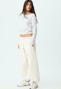 Světlý šedý dlouhý rukáv cropped top spárovaný se širokými krémovými tepláky. Kalhoty mají boční kapsy a uvolněný střih. Bílé tenisky.