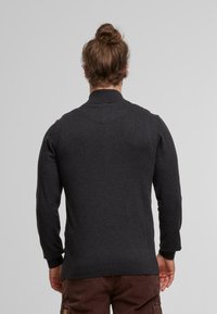 Dunkelgraues Langarm-Poloshirt mit hohem Kragen, gerippten Ärmelbündchen und strukturiertem Stoff. Getragen mit braunen Cordhosen.