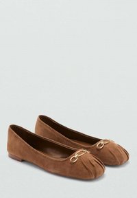 Bruine suède ballerina's met een ronde neus, een geplooid ontwerp en een gouden kettingaccent aan de voorkant. Platte zool met een minimale hak.
