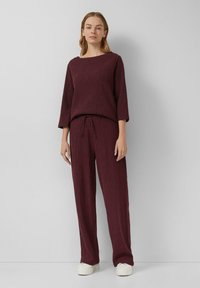 Bordeaux, textuur gebreid twee-delig outfit met een ruime halslijn top en een drawstring, losse broek. Gecombineerd met witte schoenen.
