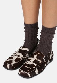 Loafers w wzmocnionym wzorem w brązowo-białe plamy, wykonane z teksturowanych materiałów, z płaską podeszwą i usztywnioną konstrukcją, w połączeniu z ciemnymi, prążkowanymi skarpetami.