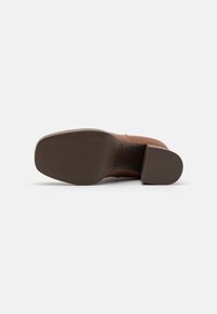 Brown leather heeled boot with a square toe, textured rubber sole, and a smooth finish. The heel is block-shaped and approximately 5 cm.